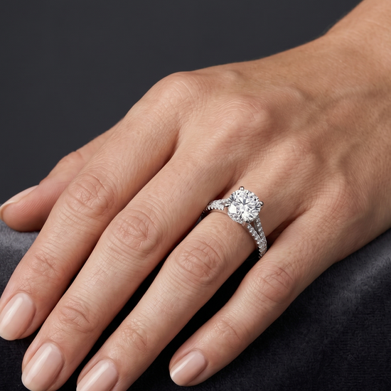 A close-up of a woman's hand resting gracefully on a dark gray surface, wearing a silver engagement ring with a large round center diamond and a diamond-encrusted band.
