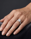 A close-up of a woman's hand resting gracefully on a dark gray surface, wearing a silver engagement ring with a large round center diamond and a diamond-encrusted band.