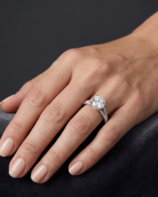 A close-up of a woman's hand resting gracefully on a dark gray surface, wearing a silver engagement ring with a large round center diamond and a diamond-encrusted band.