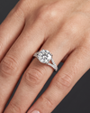 Close-up of a woman's hand resting elegantly against a dark charcoal background, wearing a white gold engagement ring with a round center diamond and a diamond-encrusted split-shank band.